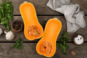 Winter squash wonders: a butternut squash cut in half on a wooden table with herbs, garlic and spices.
