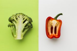 Heirloom vs. hybrid: half a head of broccoli on a green background beside a halved red pepper on white.