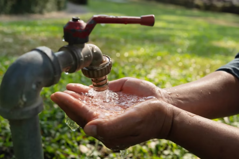 Drought tolerant gardening starts with every drop: hands catching water from an outdoor faucet.
